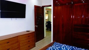 A bedroom with a wooden dresser, a bed with a patterned bedspread, a television on the wall, and a wooden wardrobe. - Unlimited Luxury Villa  LOS TULES (Puerto Vallarta)