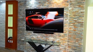 A flat-screen TV mounted on a textured wall with a glass table below. - Unlimited Luxury Villa  LOS TULES (Puerto Vallarta)