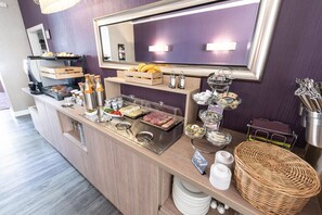 A buffet counter with various food items, a mirror, and a wicker basket. - Hotel Porta Nigra (Trier)