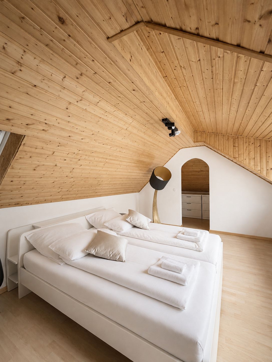 A modern bedroom with a sloped ceiling, a bed with white linens, and a lamp.