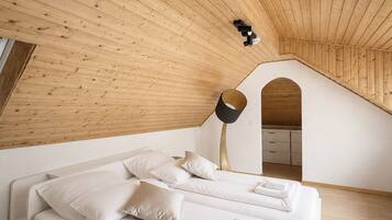 A modern bedroom with a sloped ceiling, a bed with white linens, and a lamp.