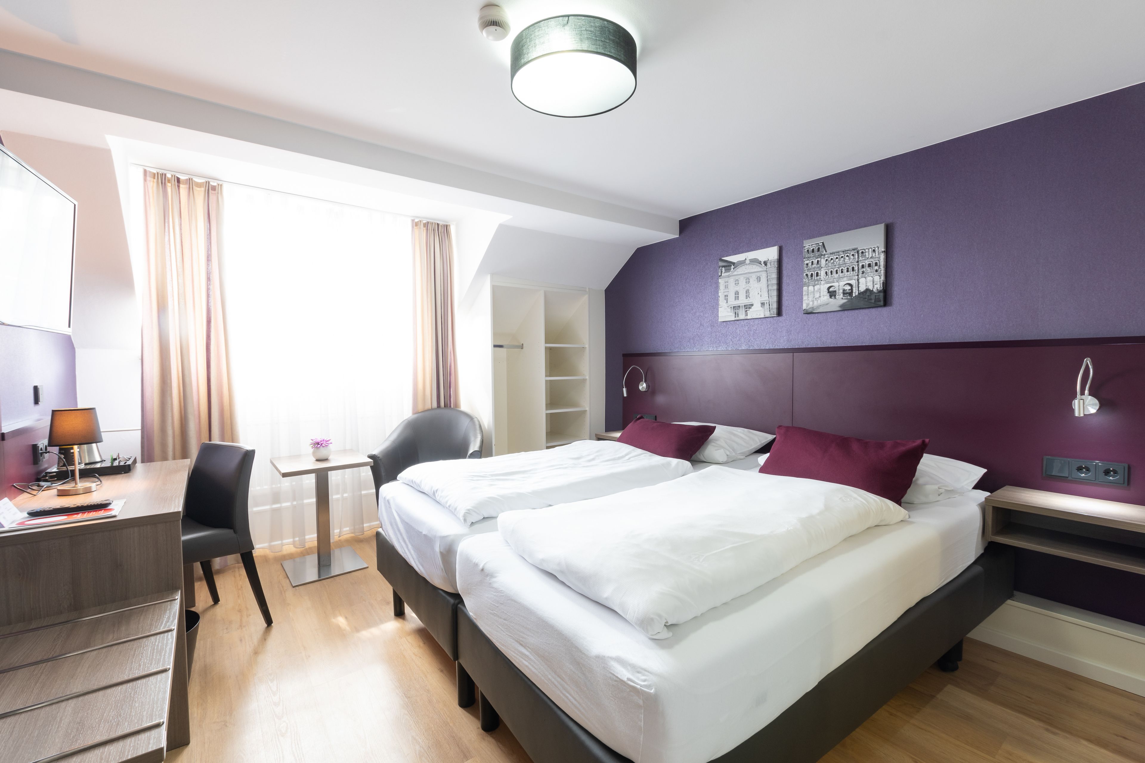 Habitación de hotel con dos camas, un escritorio, una silla y una ventana con cortinas.