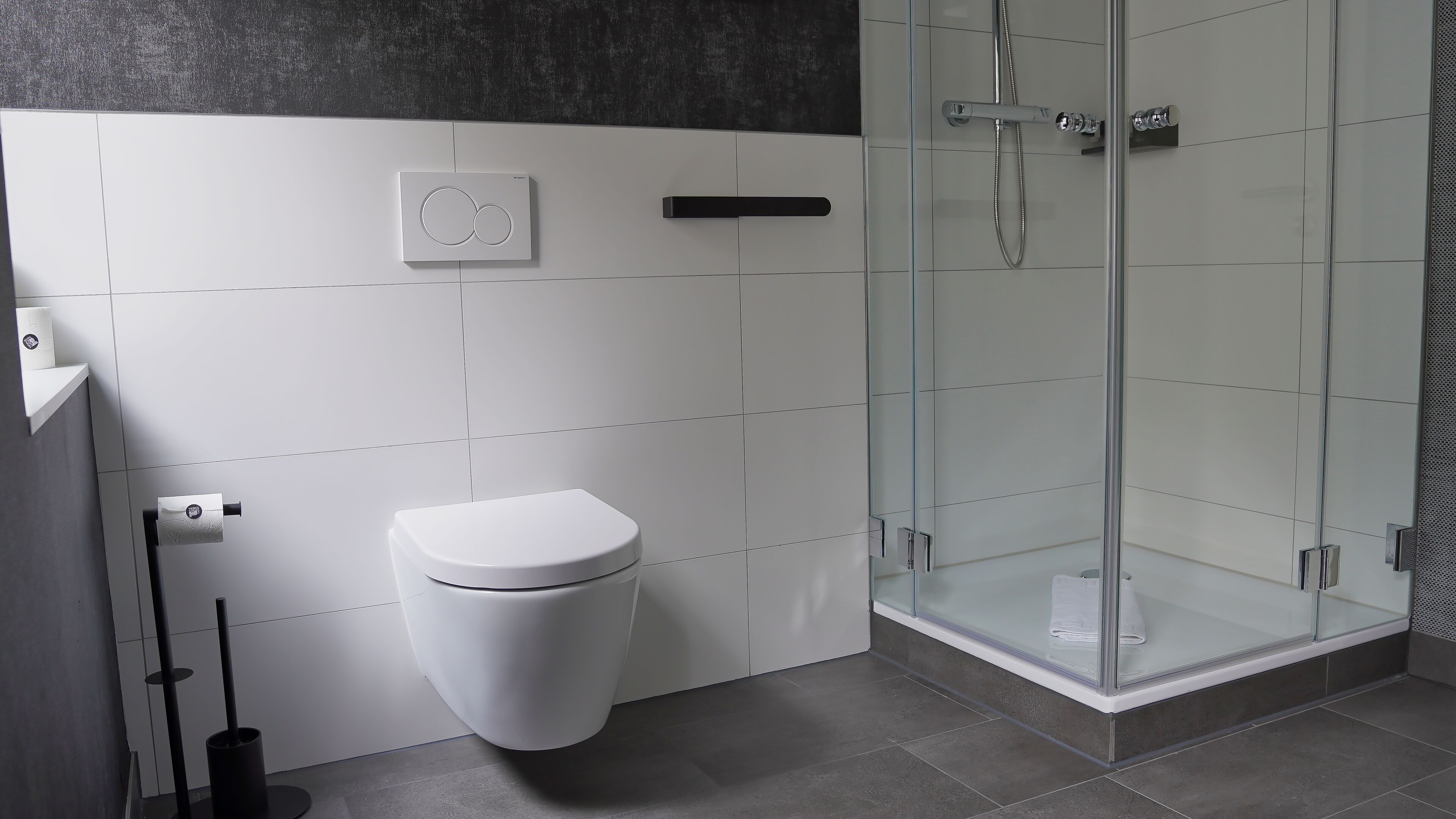 A modern bathroom with a toilet, a glass shower enclosure, and a towel rack.