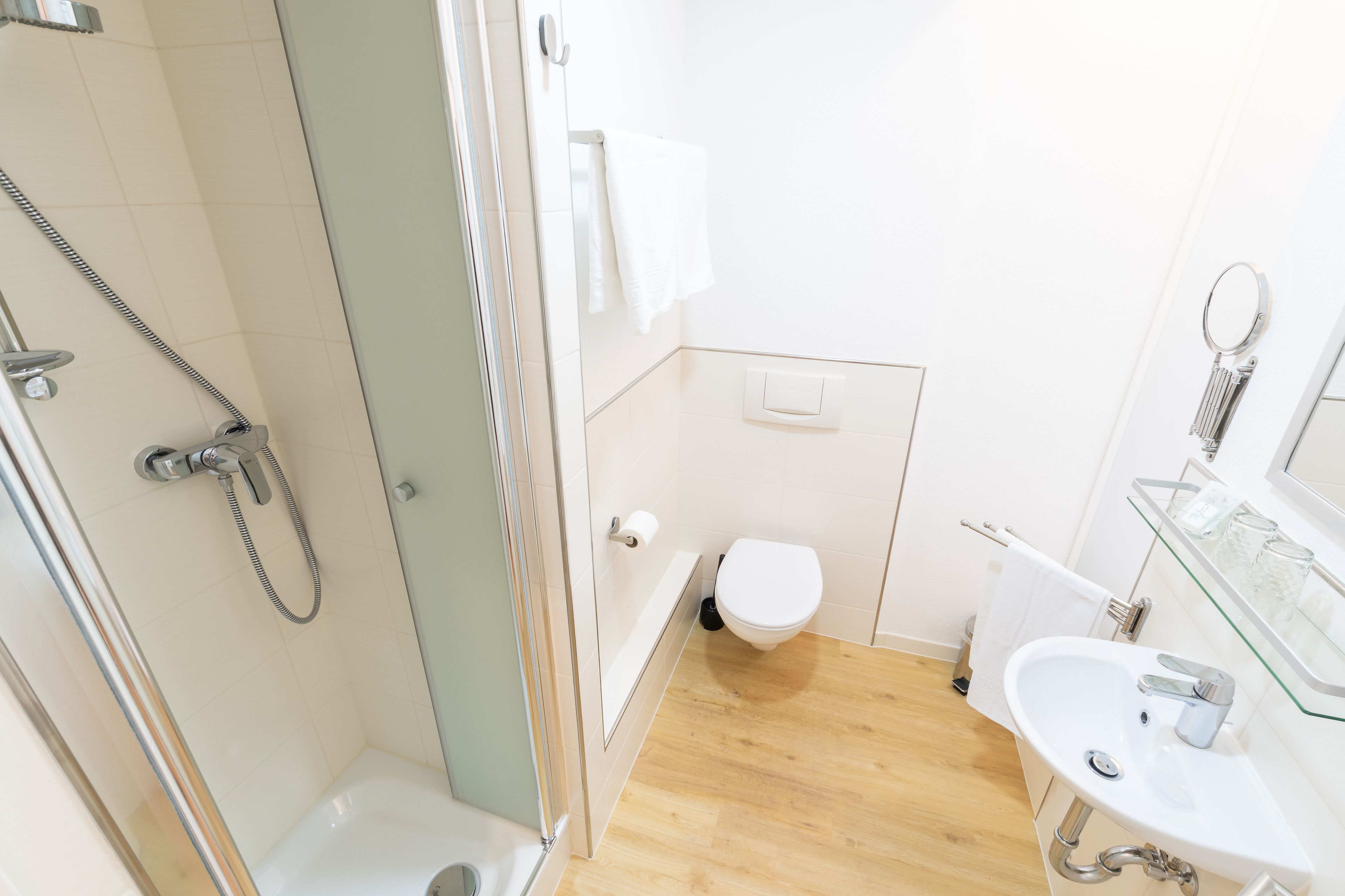 A modern bathroom with a glass-enclosed shower, a white toilet, a sink with a glass shelf, and a mirror.