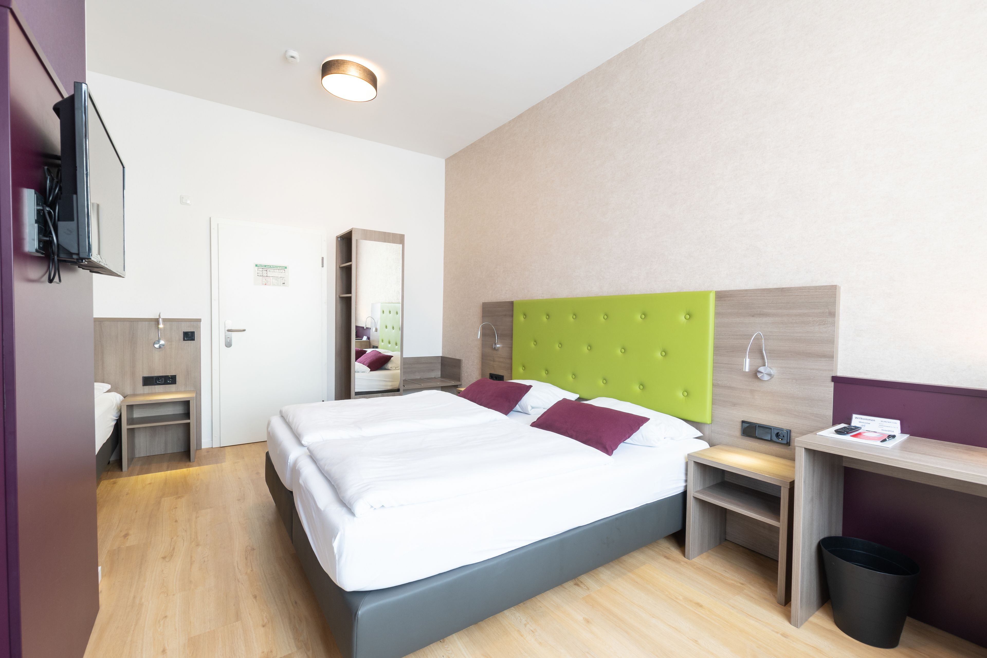 Une chambre d’hôtel moderne équipée d’un grand lit, d’un bureau, d’un miroir et d’une poubelle.