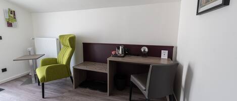 A room with a desk, two chairs, a radiator, a small table, and a framed picture on the wall.