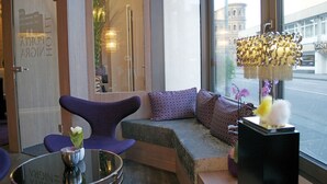 Un moderno vestíbulo de hotel con una zona de estar, una mesa de vidrio con un florero y vistas a un edificio.