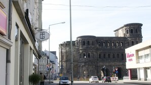 A street view with a hotel sign, a historic building, and a modern building with a sign. - Hotel Porta Nigra (Trier)