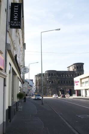 A street view with a hotel sign, a historic building, and a modern building with a sign. - Hotel Porta Nigra (Trier)