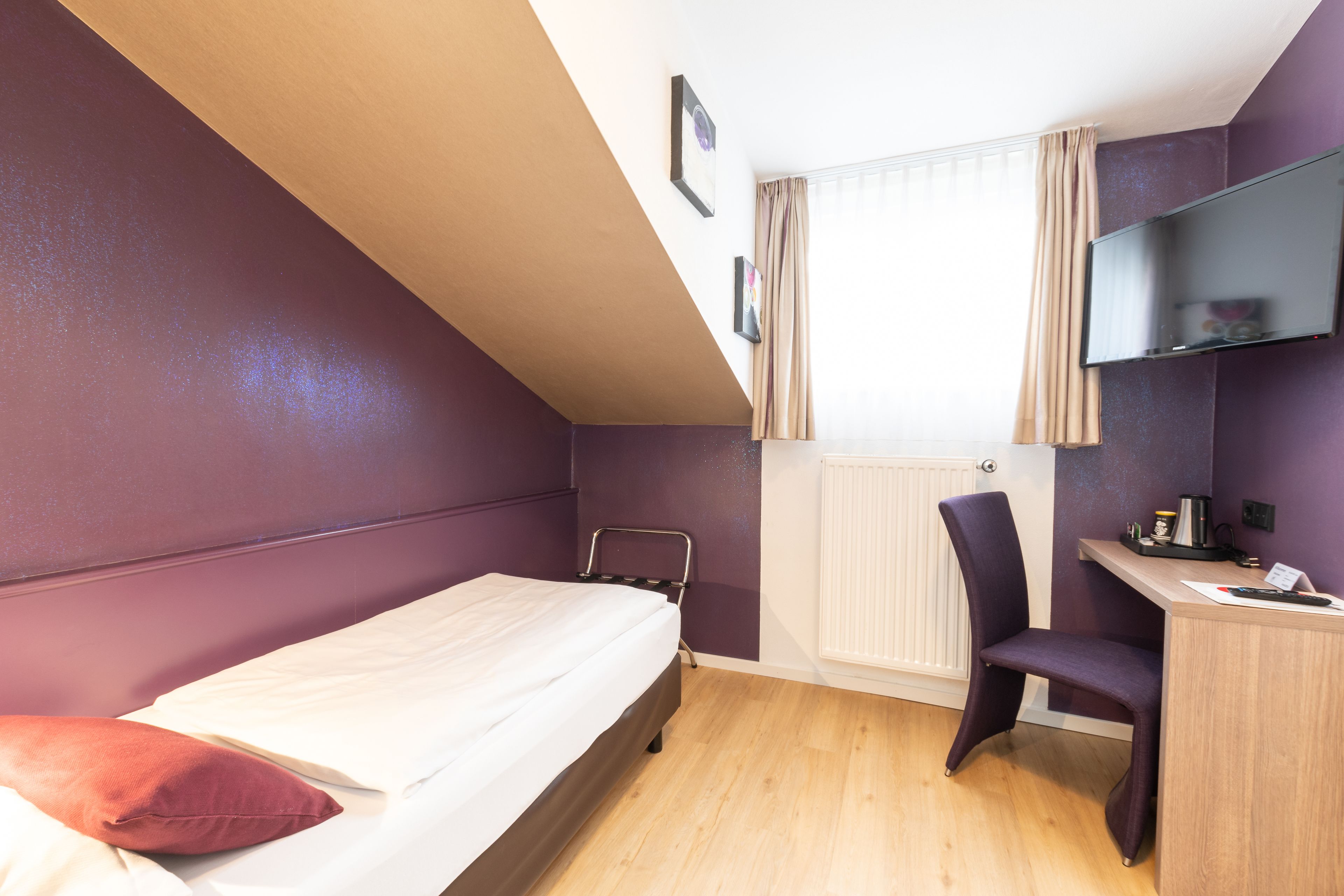 Un dormitorio con cama, escritorio, silla, radiador y televisor montado en la pared.