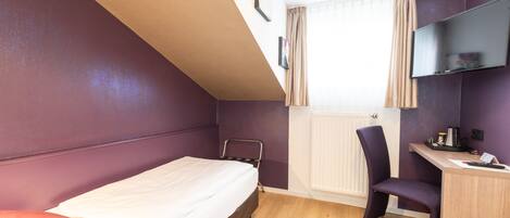 Un dormitorio con cama, escritorio, silla, radiador y televisor montado en la pared.