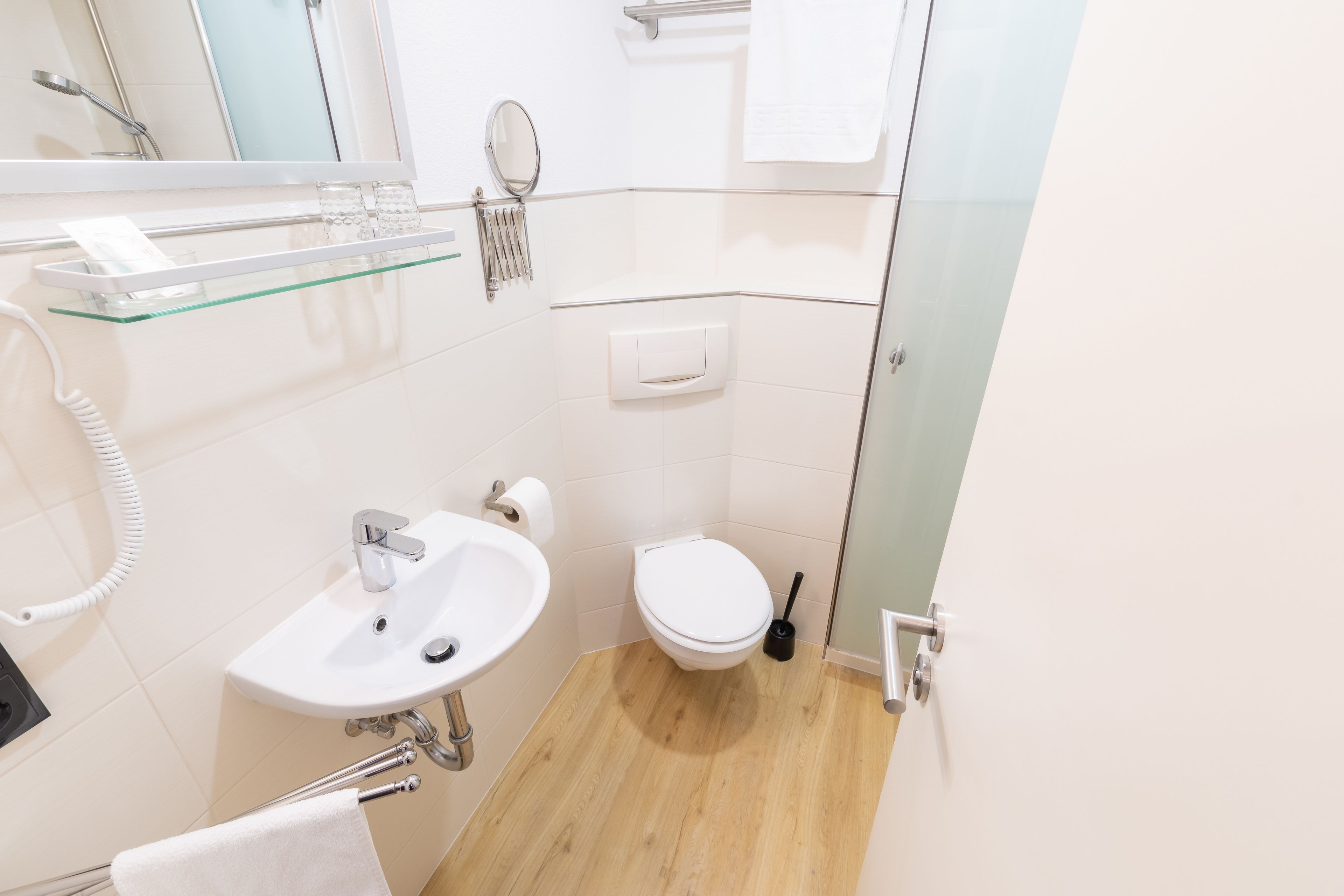 A modern bathroom with a glass shelf, white sink, toilet, and a hand dryer.