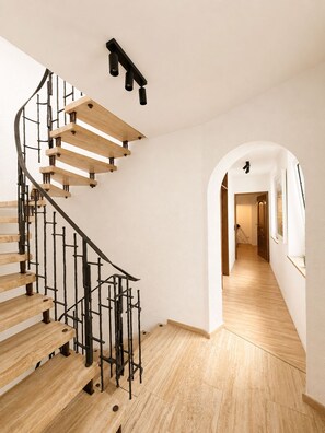 A spiral staircase with wooden steps and black metal railings, leading to a hallway with wooden flooring and white walls. - Hotel Porta Nigra (Trier)