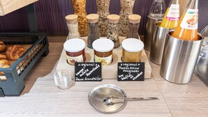 A variety of food items and condiments on a wooden table, including jars of preserves, bottles of orange juice, and a basket of croissants. - Hotel Porta Nigra (Trier)