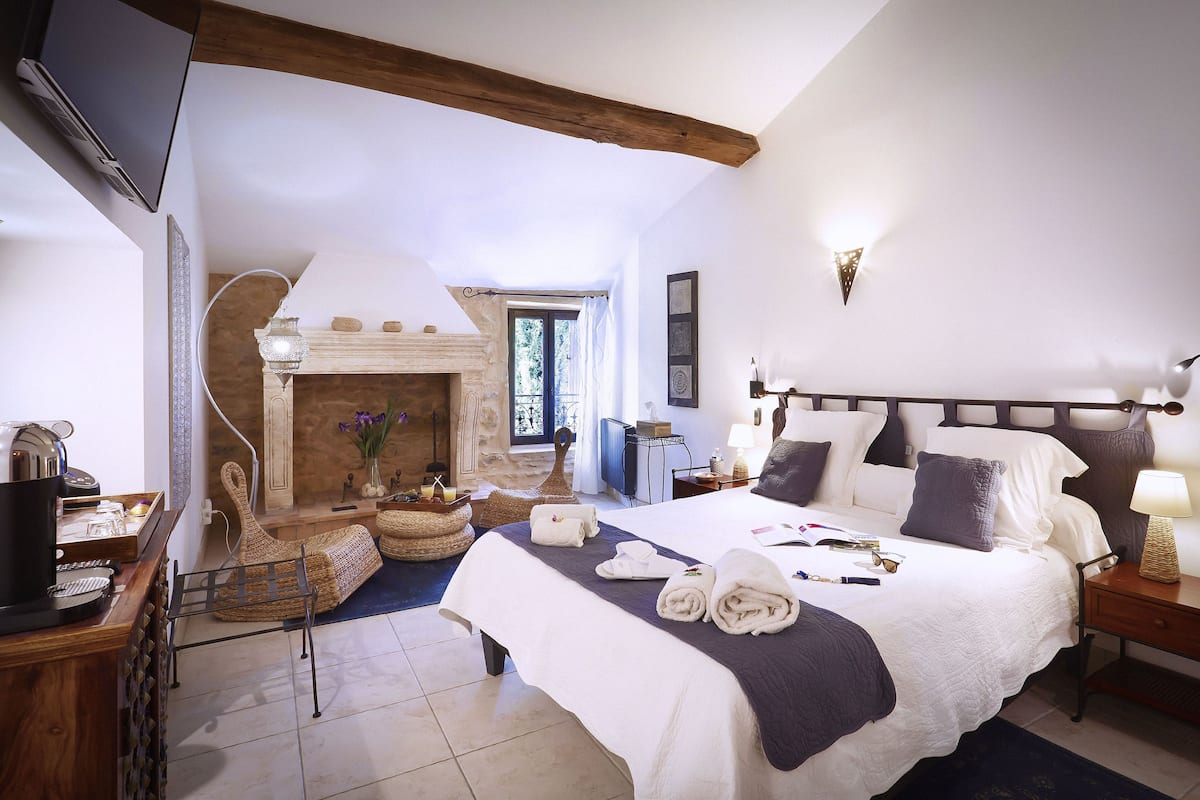 A bedroom with a bed, bedside table, lamp, and a fireplace.