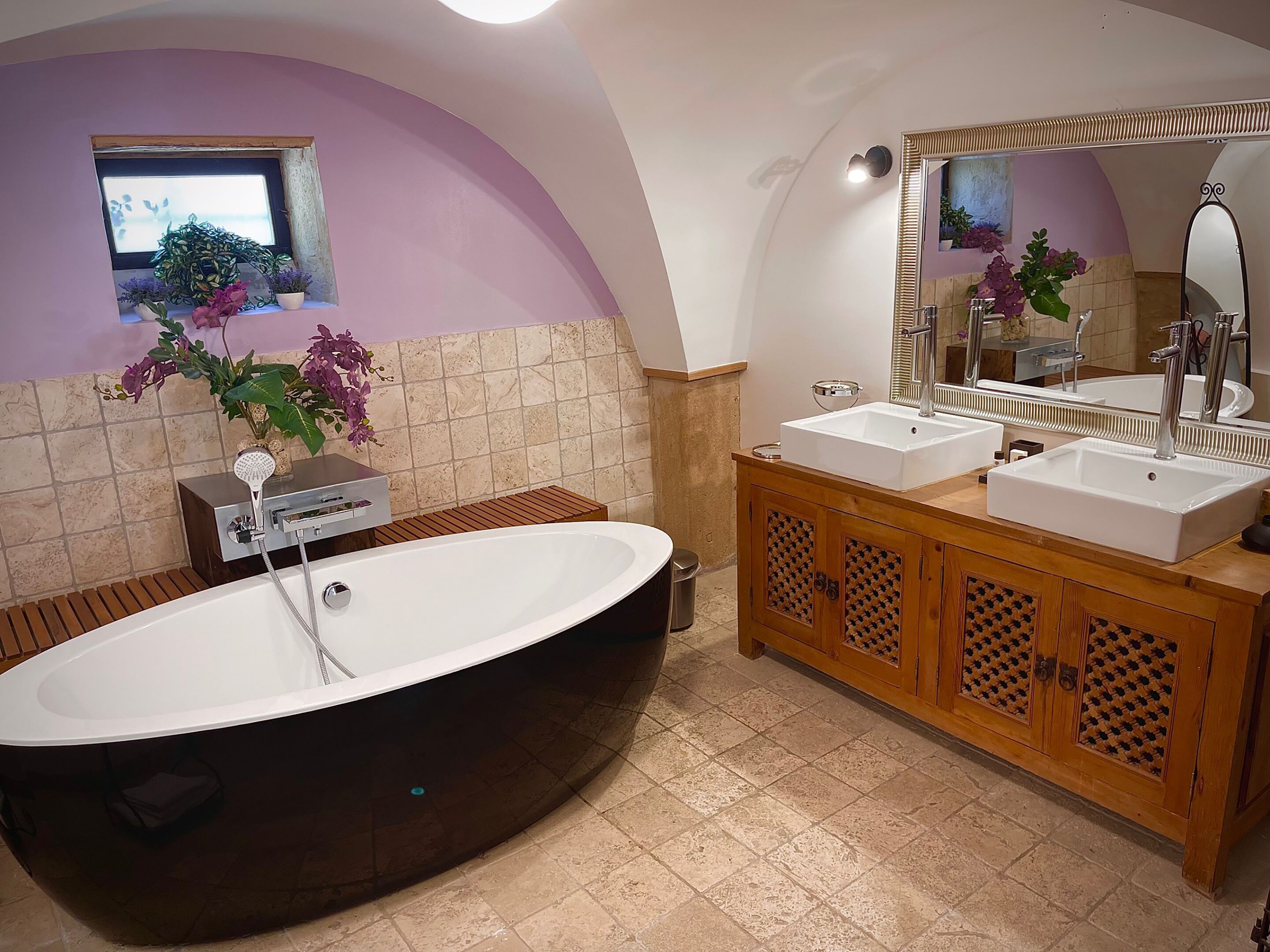 Une salle de bain avec une baignoire sur pieds, deux lavabos, un meuble-lavabo avec un miroir et des plantes en pot.