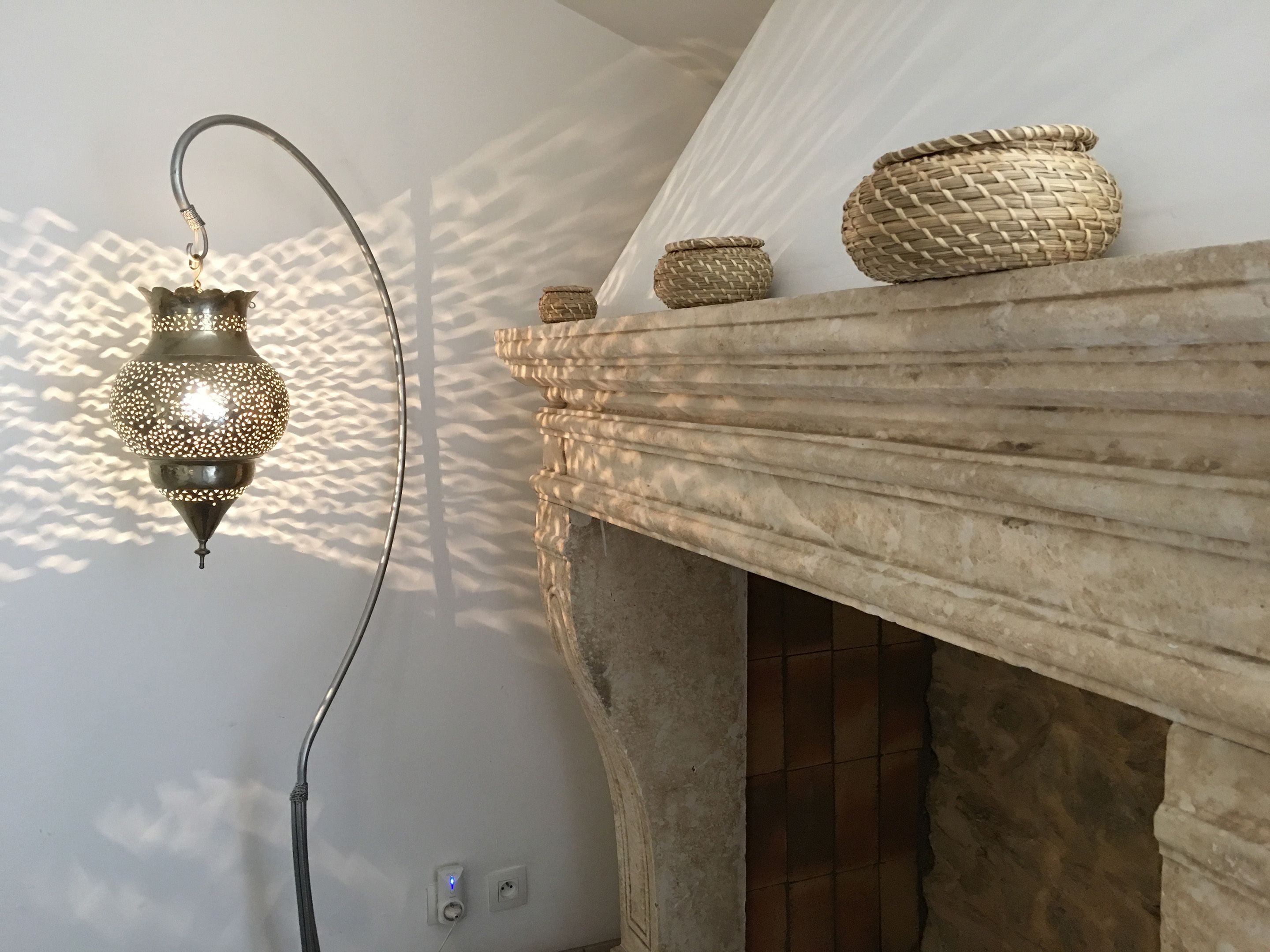 Ein Zimmer mit einer dekorativen Pendelleuchte, einem Kamin aus Stein mit gewebten Körben darauf und einer gefliesten Wand.