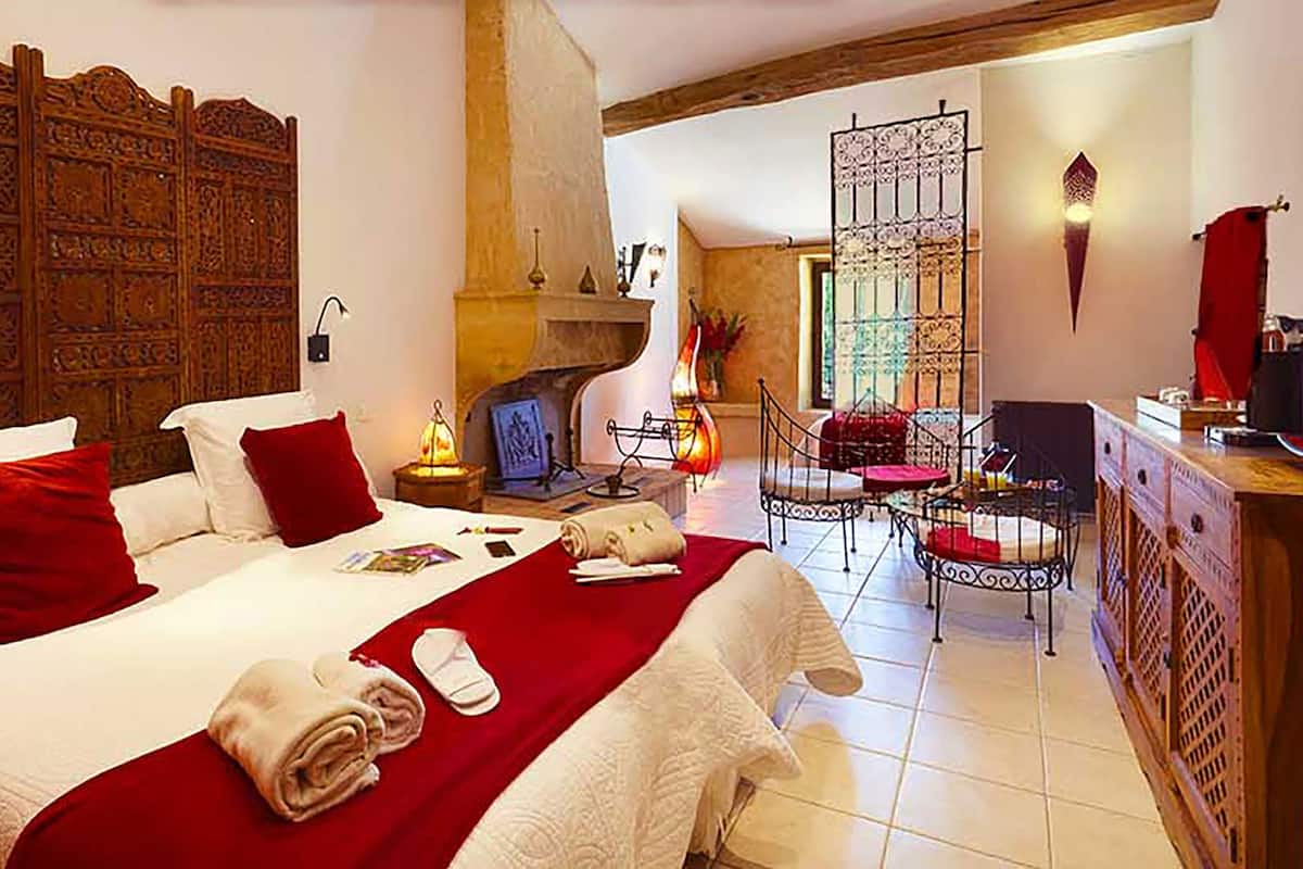 A hotel room with a large bed, a fireplace, a dining area, and a decorative wall.
