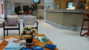 Un hall d’hôtel avec un comptoir d’accueil, des chaises, une table avec des magazines et un vase de fleurs.