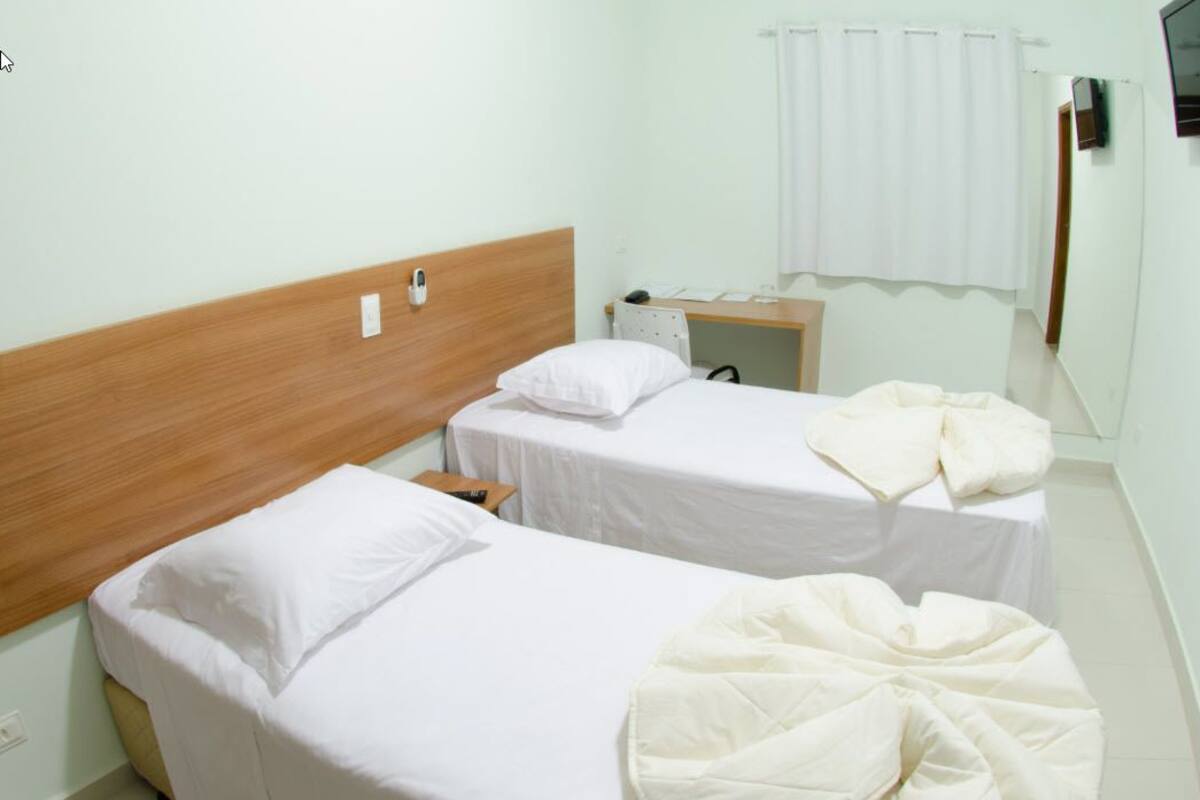 A hotel room with two single beds, a wooden headboard, a small desk, and a mirror.