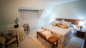 Une chambre à coucher comprenant un lit, des tables de chevet, une chaise, une petite table avec une plante et une fenêtre avec des rideaux.