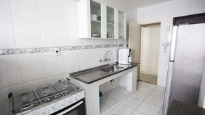 Una cocina con armarios blancos, estufa a gas, pileta y refrigerador.