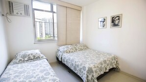 Un dormitorio con dos camas individuales, una ventana con persianas, un radiador y dos cuadros en la pared.
