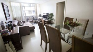 Una sala de estar moderna con un sofá, una mesa de comedor con sillas, un televisor y una planta en maceta.