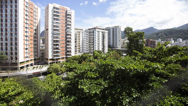 Un edificio residencial alto con varios balcones, rodeado de exuberante vegetación y montañas al fondo.