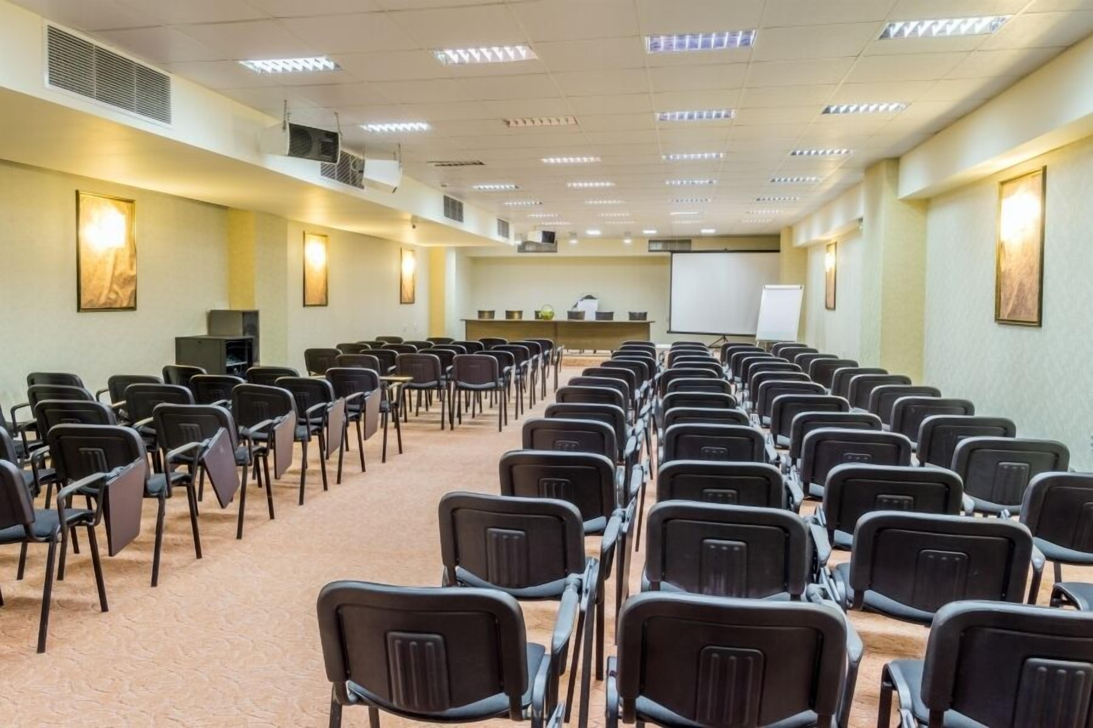 A conference room with rows of chairs, a projector screen, and a whiteboard.