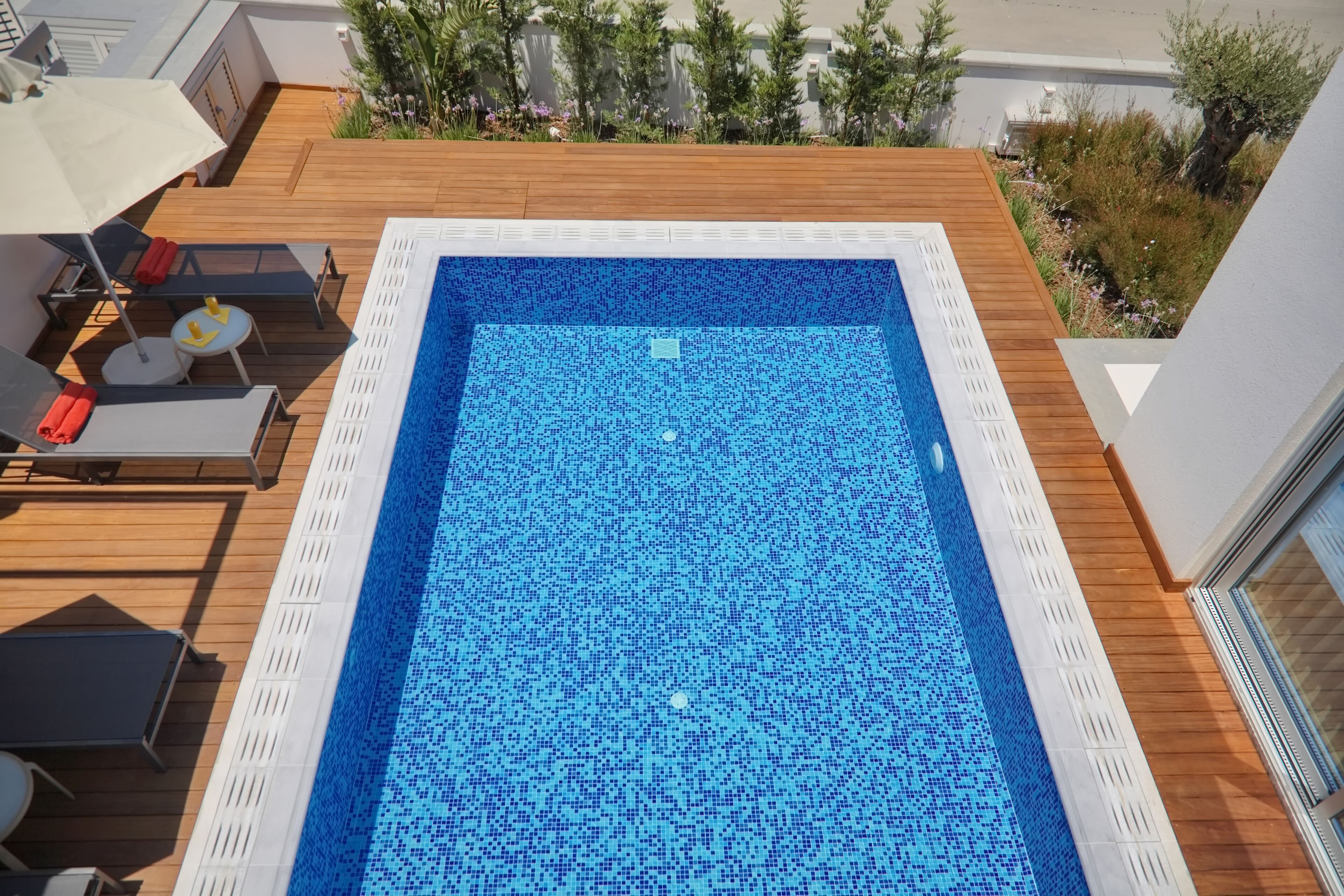 Una piscina rettangolare con un motivo a mosaico blu, circondata da un pontile in legno e ringhiere bianche.