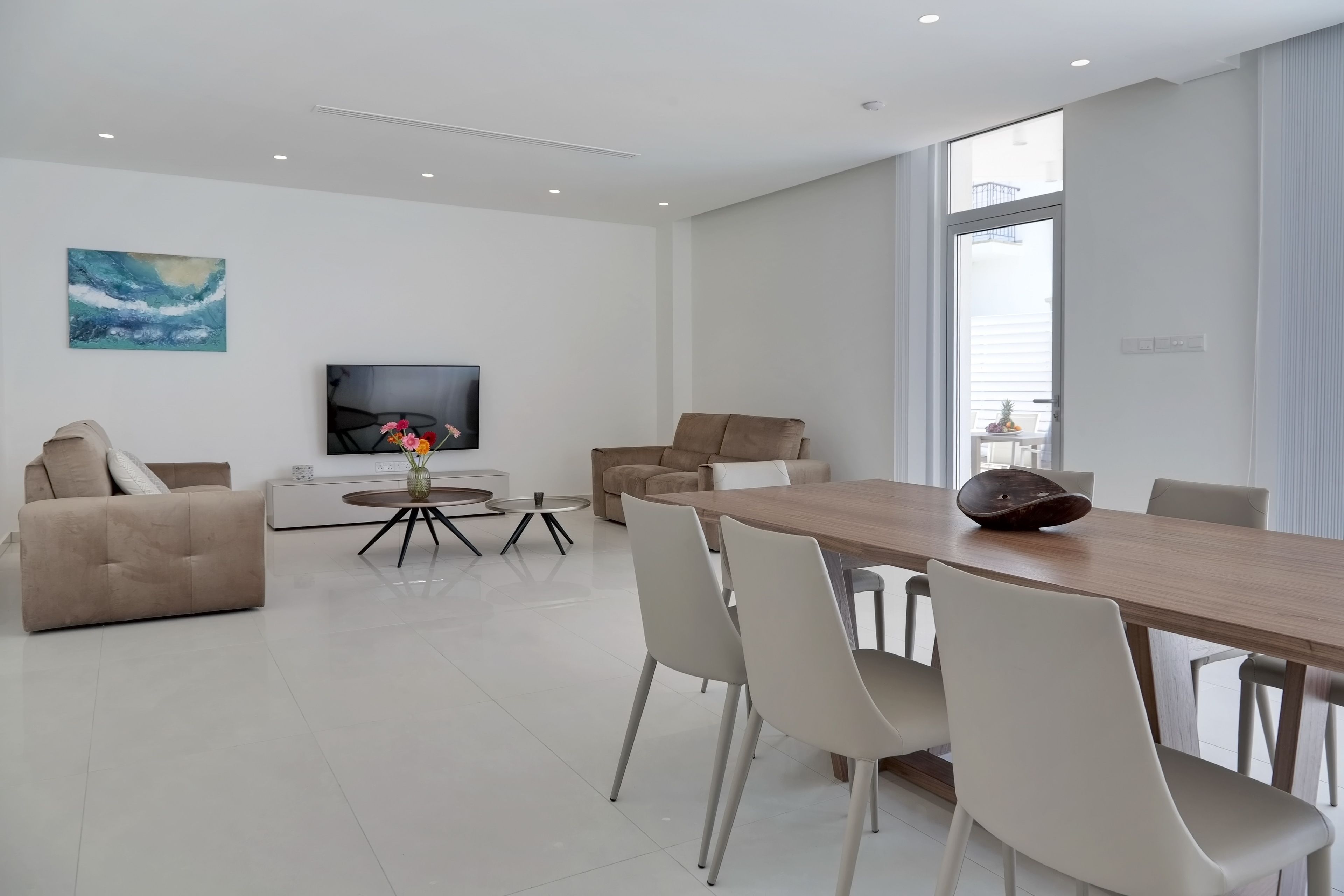 A modern living room with a sofa, a dining table with chairs, a TV, and a painting on the wall.