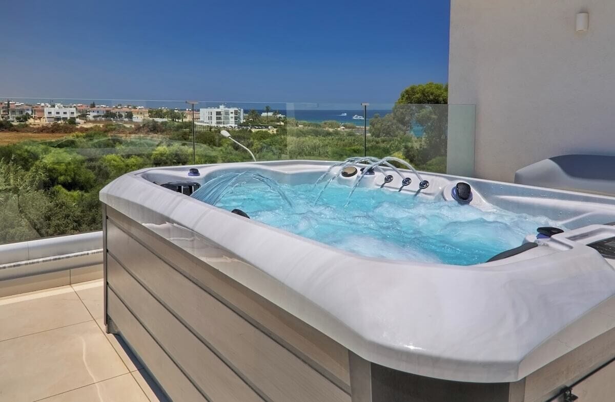A hot tub on a balcony with a view of the sea and buildings.