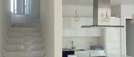 Una cocina moderna con una isla central, electrodomésticos de acero inoxidable e iluminación colgante.