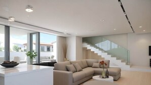 A modern living room with a large beige sectional sofa, a round coffee table, and a glass staircase. - Sunrise Seaview Villas (Paralimni)