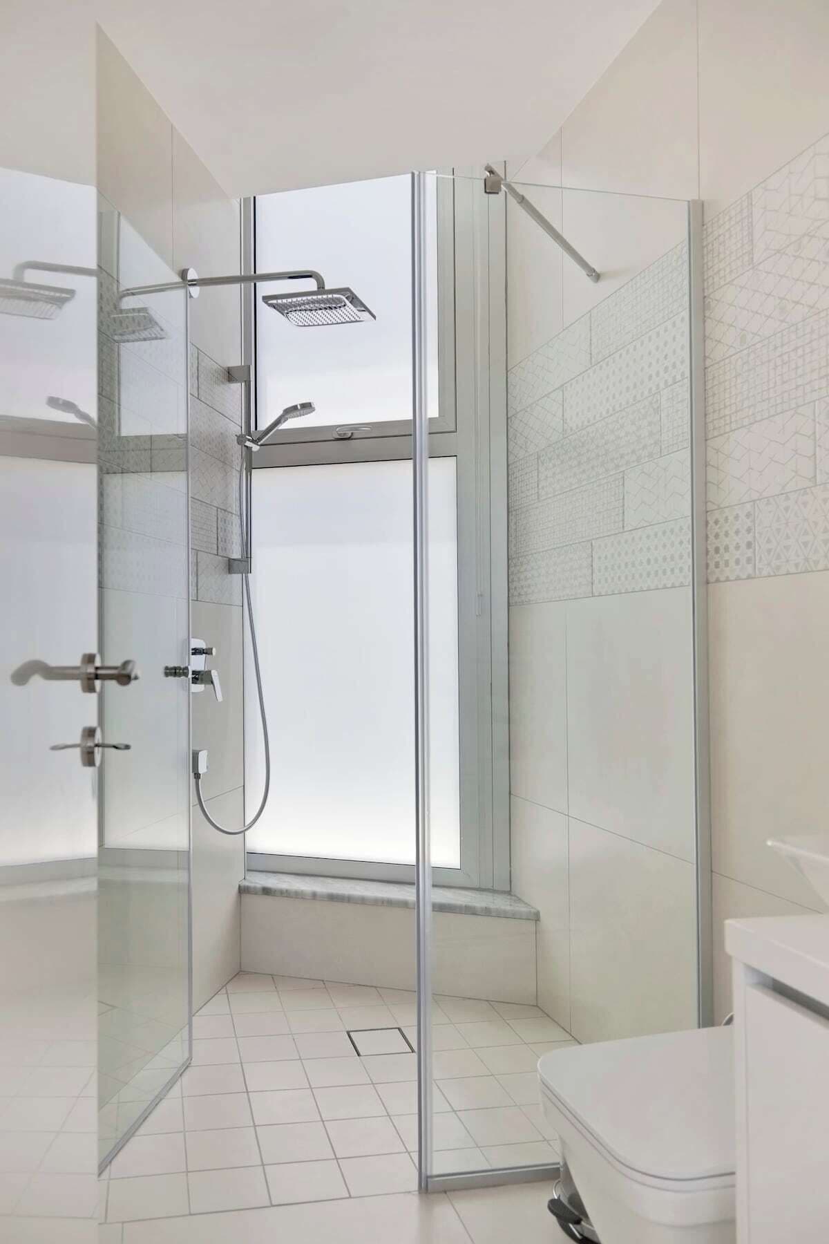 A modern bathroom with a glass-enclosed shower, white tiles, and a toilet.