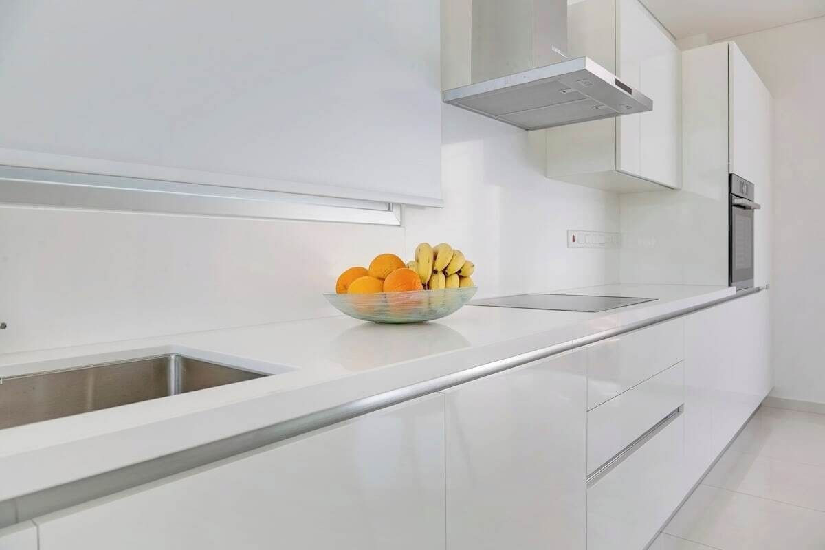 A modern kitchen with white cabinetry, a stainless steel sink, and a bowl of fruit on the countertop.