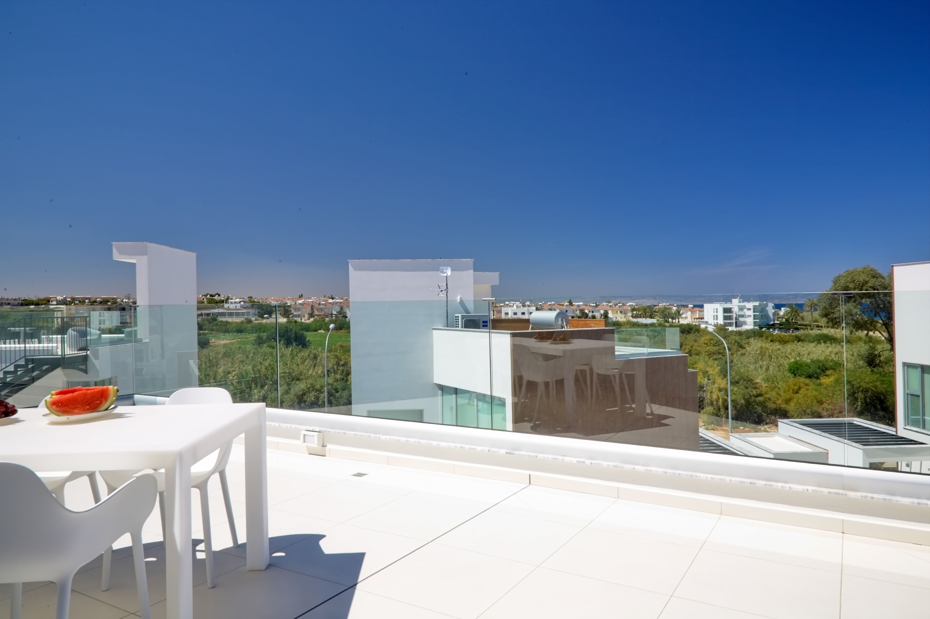 Eine Dachterrasse mit Glasgeländer, einem Tisch mit Stühlen und Blick auf die Stadtlandschaft.