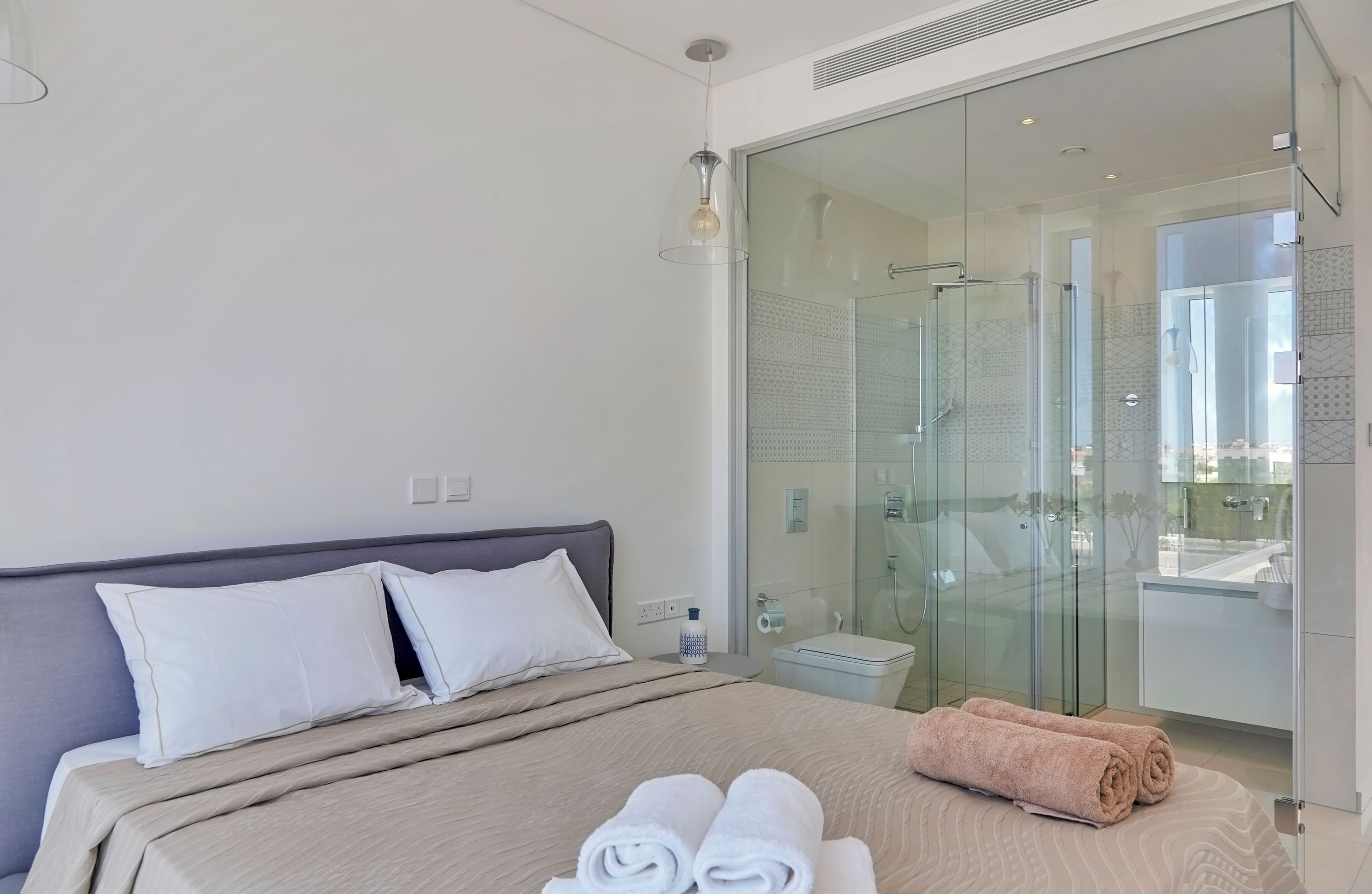 Quarto de hotel moderno com cama, box de vidro e vista para o exterior.