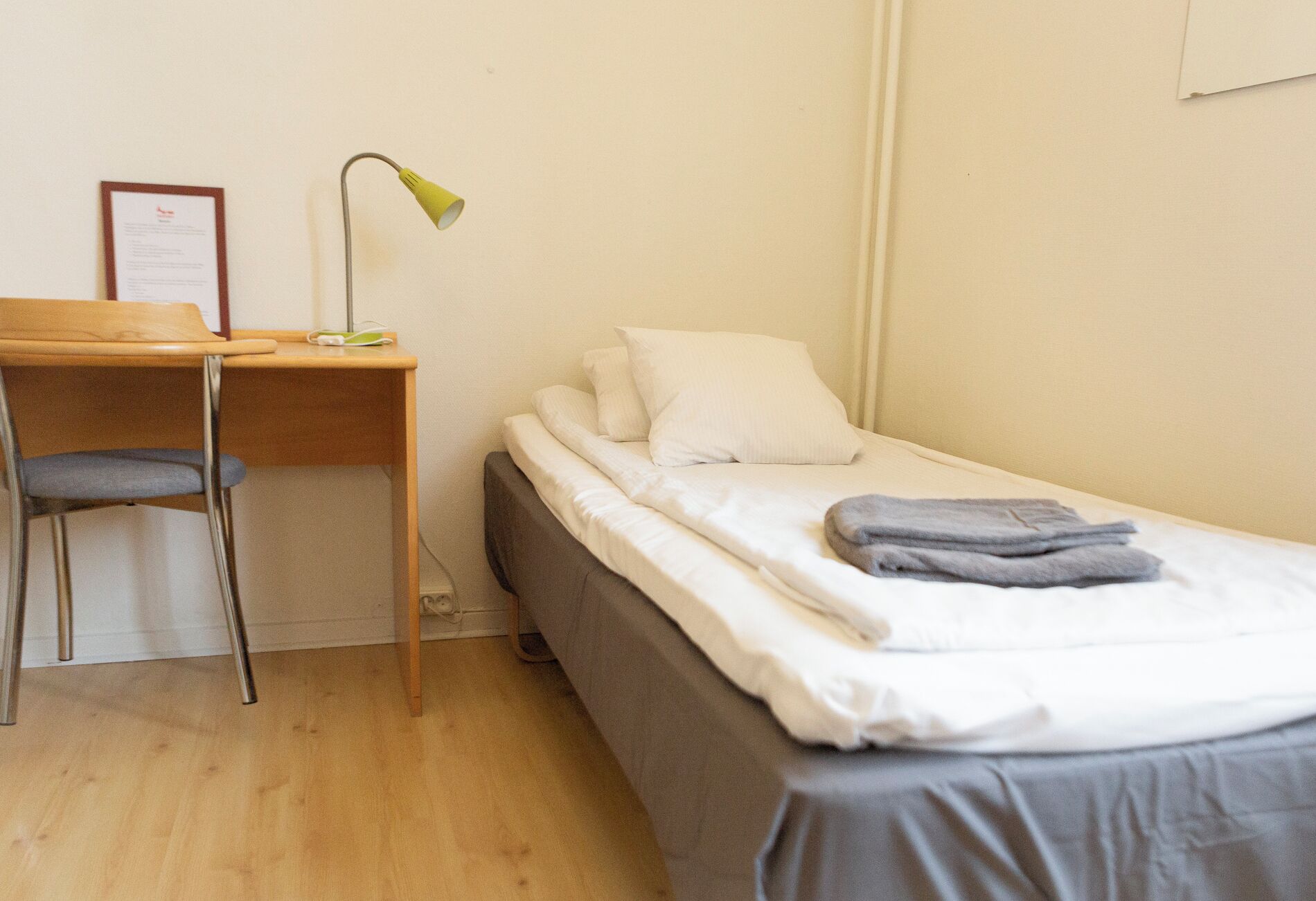 Una habitación pequeña y ordenada con una cama individual, un escritorio y una silla.