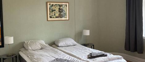 A double bed with a black frame and grey bedding, two bedside tables with lamps, a framed picture on the wall, and a window with dark curtains.