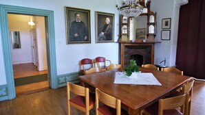 Une salle à manger avec une table en bois, des chaises et un lustre. Deux portraits encadrés ornent le mur.