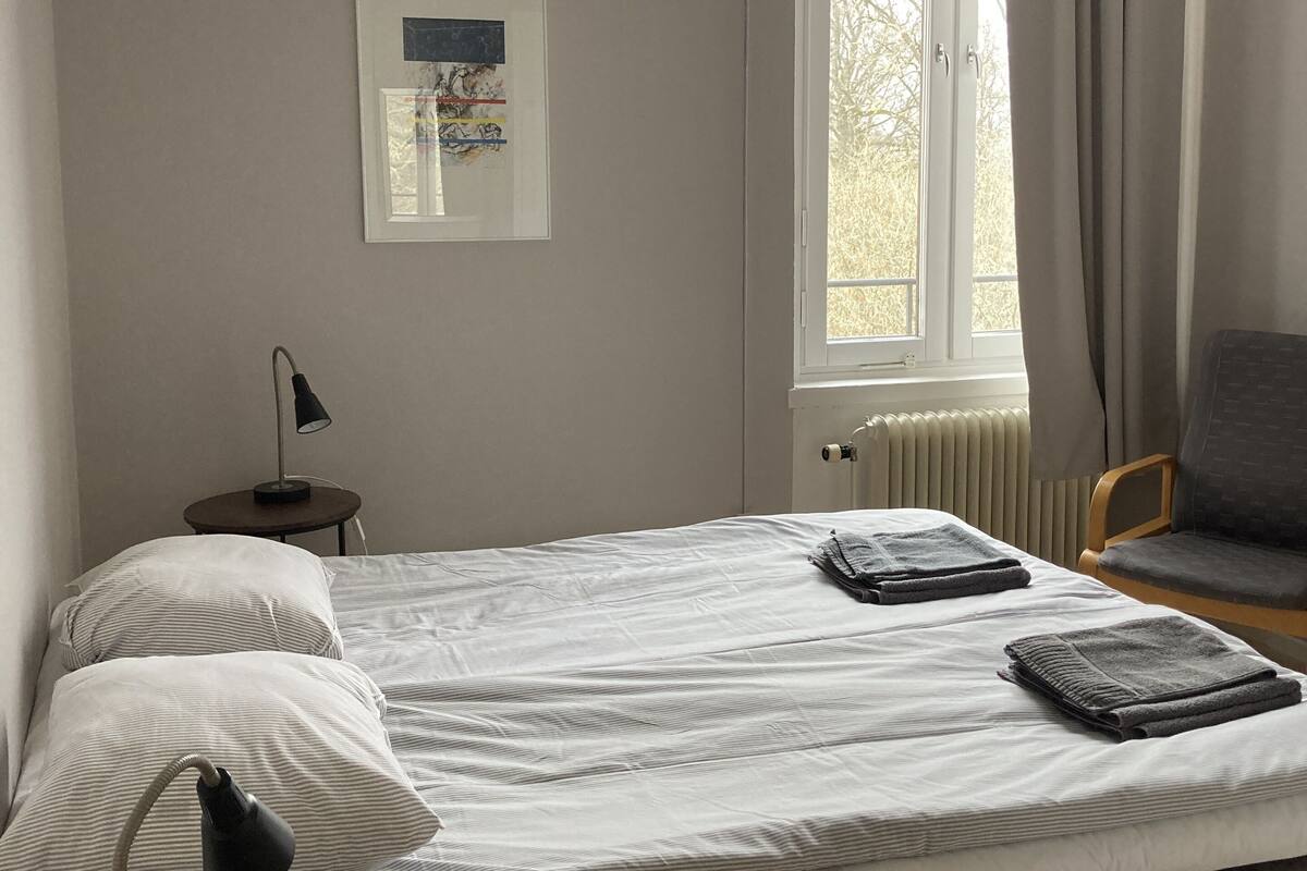Una cama bien hecha con edredón a rayas, una lámpara de noche y un cuadro en la pared.