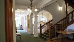 Un vaste hall d’entrée avec un escalier, des colonnes en bois et un lustre.