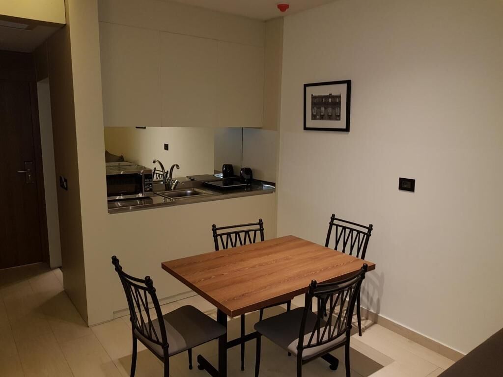 Une cuisine de taille réduite avec une table en bois et quatre chaises, un petit plan de travail avec un évier et un tableau encadré au mur.