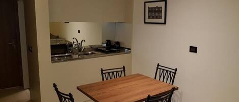 Une cuisine de taille réduite avec une table en bois et quatre chaises, un petit plan de travail avec un évier et un tableau encadré au mur.