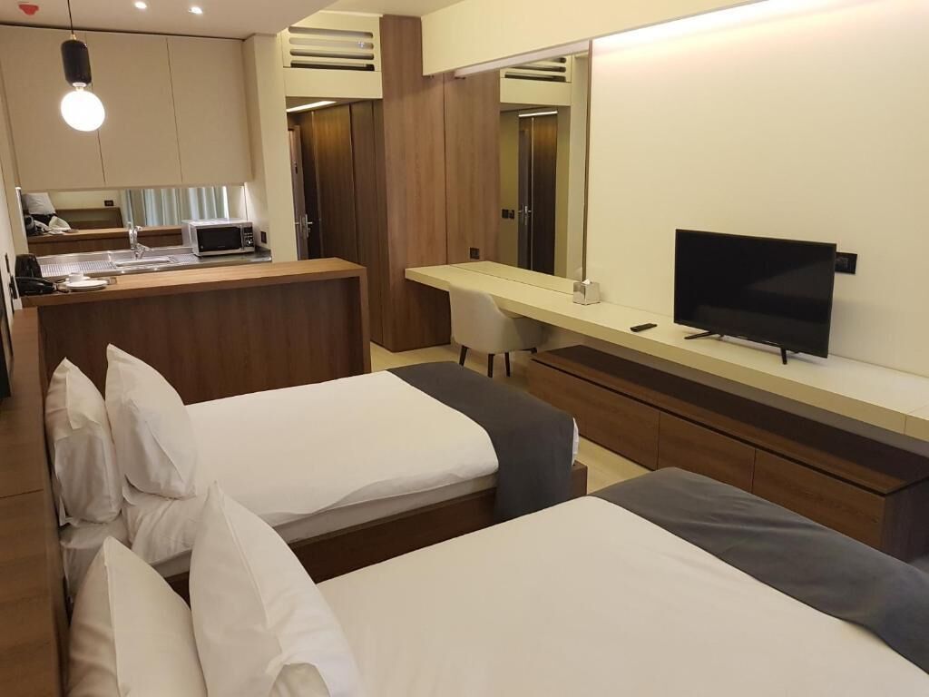 A hotel room with two beds, a desk with a computer, a TV, and a mirror.