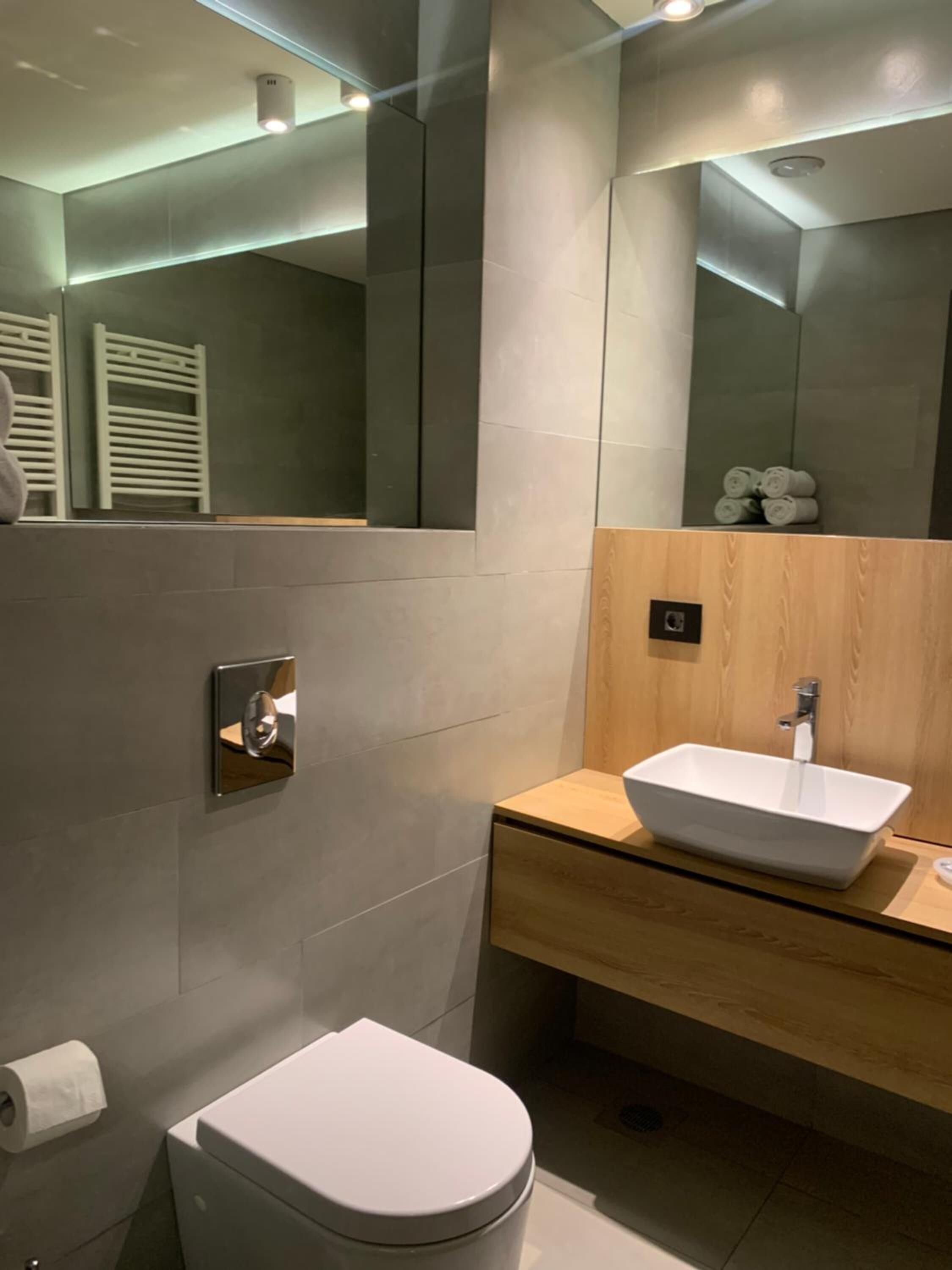 A modern bathroom with a white toilet, a wooden vanity with a white sink, and a large mirror.