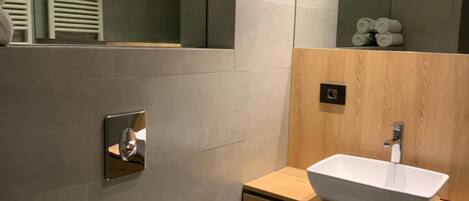 A modern bathroom with a white toilet, a wooden vanity with a white sink, and a large mirror.