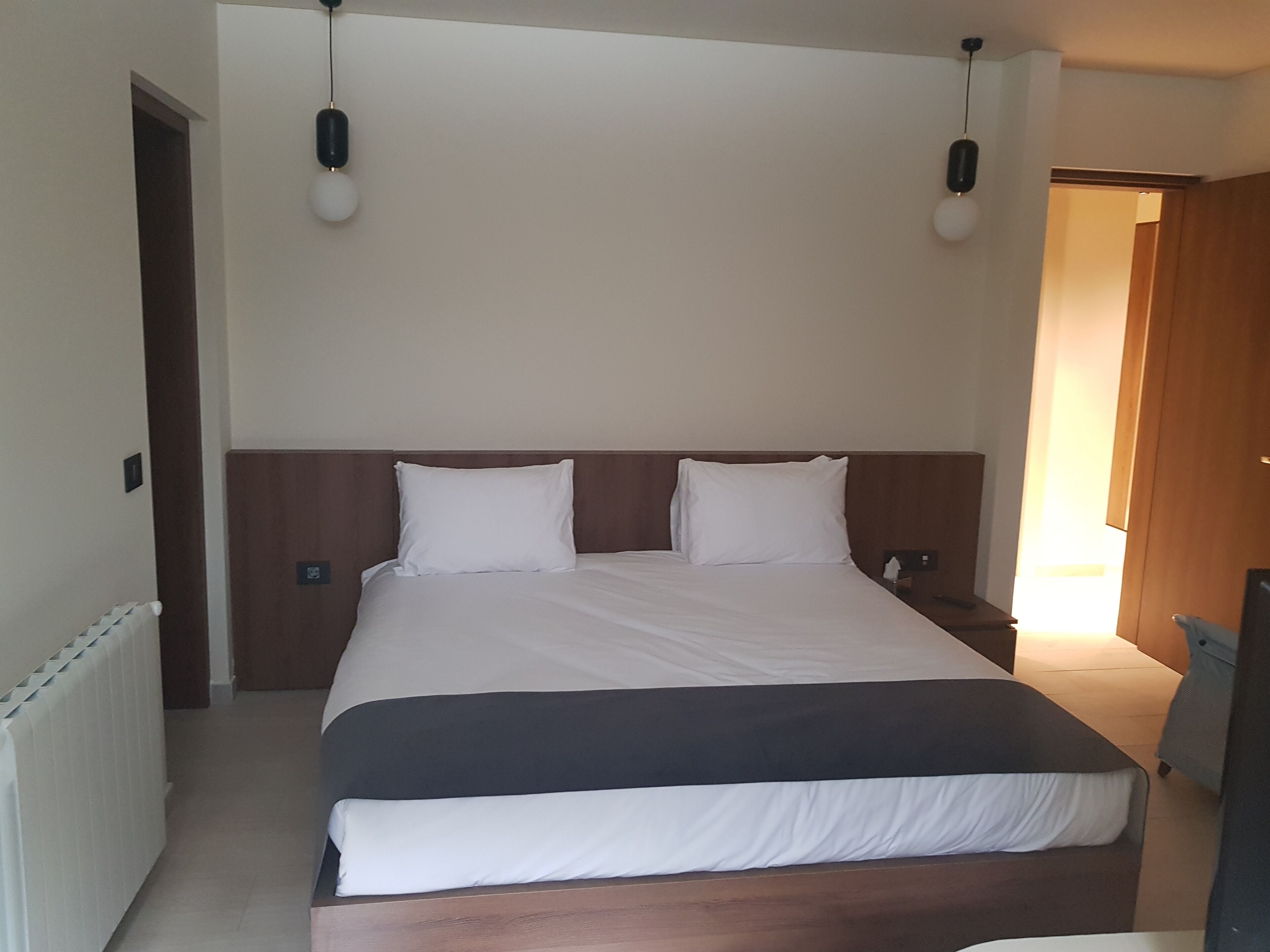 A hotel room with a large bed, a wooden headboard, two bedside lamps, and a radiator on the left.